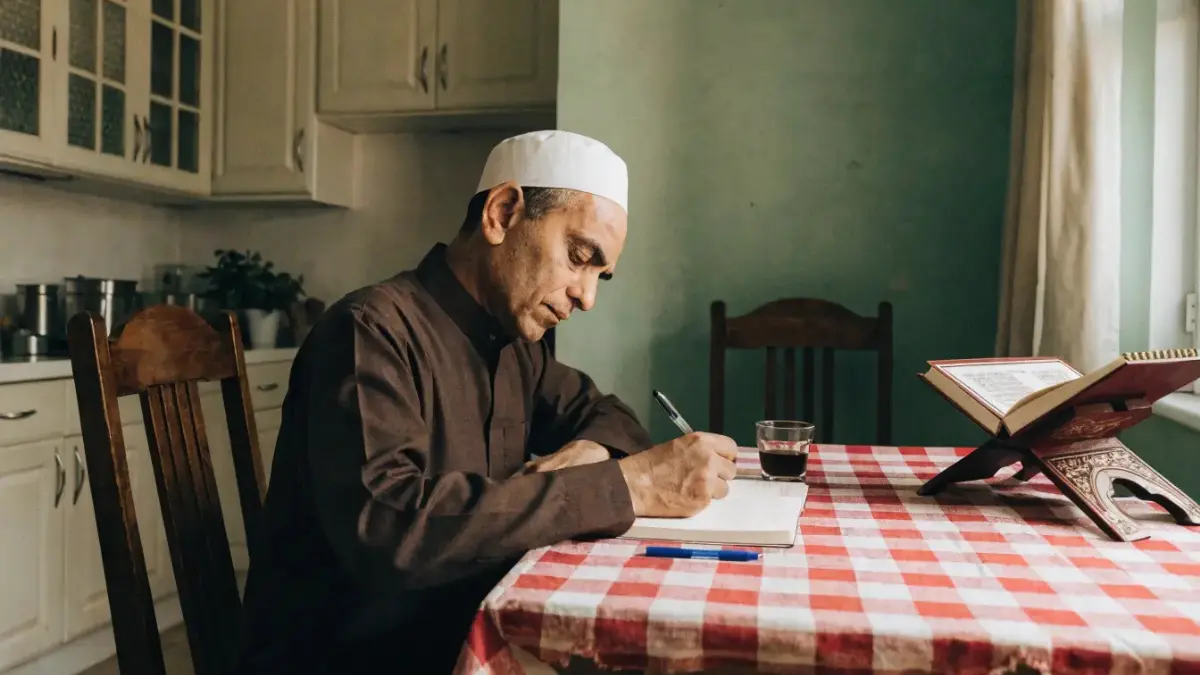 Un homme assis à un bureau en bois avec un carnet et un Coran pour sa routine ramadan